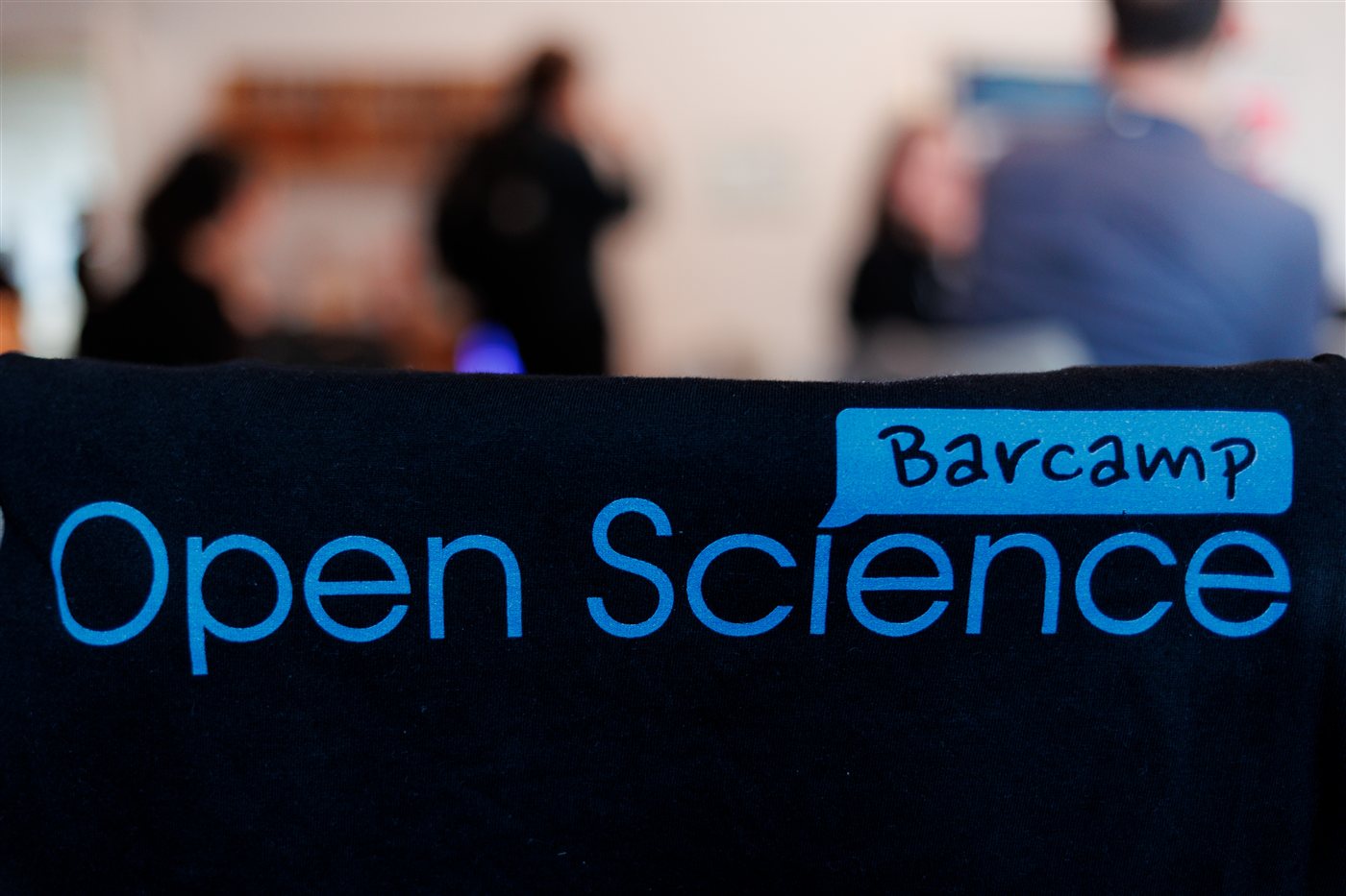A Barcamp Open Science t-shirt in the foreground with participants talking in the background.